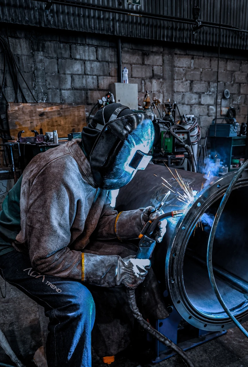 Fabricator TIG-welding a flanged steel pipe spool in the workshop